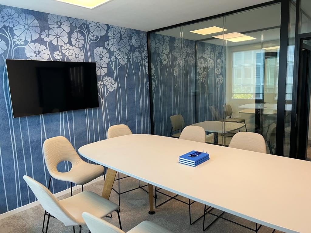 Salle de conférence 7 personnes — papier peint bleu floral, cloisons vitrées, table ovale, Genève 2023