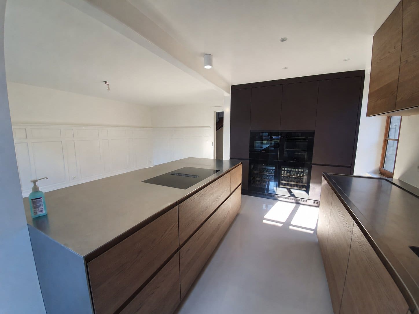 Cuisine maison de village — îlot plan inox, façades chêne, colonnes Miele, caves à vin