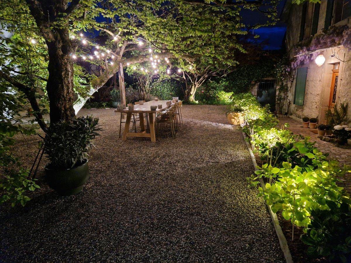 Jardin maison de village de nuit — éclairages, table sous arbres